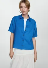 Camisa blanca de lino con cuello clásico, manga corta y cierre frontal con botones.