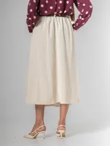 Falda midi de corderoy color beige claro, con pliegues verticales marcados y cintura elastizada. Incluye un cinturón desmontable de cuero marrón con hebilla dorada.