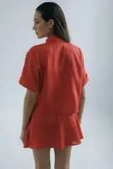 Camisa corta de manga corta color rojo, con doble cartera diagonal con botones de madera, cuello clásico y botamangas marcados. Tiene un bolsillo con aplique de crochet hecho a mano con forma de frutilla.