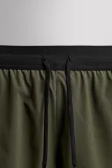 Shorts deportivos color verde oliva confeccionados en tejido técnico ligero y elástico. Cuenta con forro interior, cintura elástica ajustable con cordón, bolsillos laterales, bolsillo de seguridad en espalda con cierre de cremallera, bajo con aberturas laterales y logo estampado en la pierna.