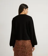 Chaqueta corta de punto color negro, con escote en V, manga larga abullonada, sisa desplazada, abotonado frontal total con botones forrados y puños acanalados.