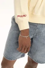 Buzo color crema de corte holgado, con cuello redondo y puños acanalados en color azul. Estampado pequeño con la frase "Karma Club" en el pecho.