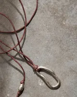 Collar con dije irregular dorado y cordón marrón ajustable.