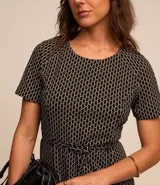 Vestido corto negro con estampado geométrico en color crema, de corte recto, manga corta y cuello redondo. Incluye cinturón fino del mismo tejido.