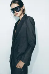 Blazer gris oscuro con cuello solapa, manga larga, bolsillos con solapa en el delantero y cierre frontal con dos botones forrados.