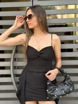 Vestido corto negro con breteles finos, escote recto y falda con volados asimétricos.
