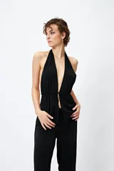Top halter negro con escote profundo y destellos metalizados. El frunce frontal realza la silueta y el tajo sutil aporta un toque atrevido.