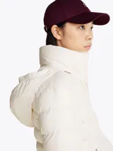 Campera Tommy Hilfiger color blanco, acolchada con plumón, de corte regular. Tiene cuello chimenea, capucha plegable, cierre de cremallera, dos bolsillos laterales con cremallera, puños elásticos con botones a presión y parche con el logo de la marca en la manga.