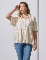 Blusa color crema de crepe con cuello a la base con solapa y escote en V con abertura central y botones. Delantera con detalles plisados y apliques en crochet. Manga corta con terminación fruncida. Ruedo en broderie.
