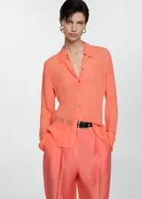 Blusa color salmón de tejido fluido semitransparente, con cuello camisero, manga larga con puños abotonados y cierre frontal con botones.