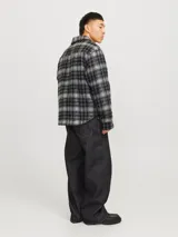 Sobrecamisa corta de manga larga con cuello sport, cierre frontal de cremallera, puños con botones, solapa cortaviento, bolsillos en pecho y delanteros. Diseño a cuadros grises y negros.