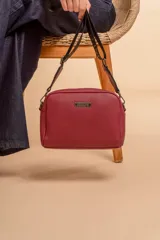 Bandolera pequeña de textura símil cuero color caramelo/marrón, con dos compartimentos principales con cierre. Correa ancha ajustable de tela negra con inscripción en relieve.