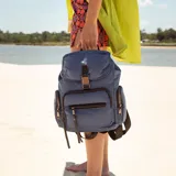 Mochila negra de nylon con tapa y broche metálico. Tiene apertura superior con broche, bolsillos internos, bolsillo con cierre metálico al frente y laterales. Tiene asas rígidas de mano y correas regulables para colgar en la espalda.