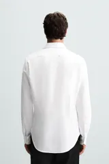 Camisa blanca de manga larga con cuello italiano abierto y puños abotonados. Presenta un corte slim fit y cierre frontal de botonadura.