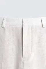 Pantalón de corte relajado confeccionado en tejido de lino color beige claro. Cuenta con cintura elástica, bolsillos frontales, bolsillos traseros de plastrón y cierre frontal con cremallera y botón.