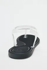 Sandalia plana con tiras de vinilo transparente y suela negra.