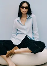 Camisa celeste de lino con cuello camisero, manga larga con puños abotonados y cierre frontal con botones.
