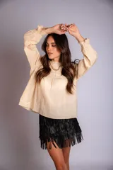 Camisa color crema con cuello alto y mangas largas con volados en los puños. Presenta detalles de crochet y broderie en el frente.