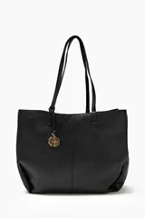 Cartera tote negra de cuero sintético con doble asa de hombro y dije metálico circular con el nombre de la marca.