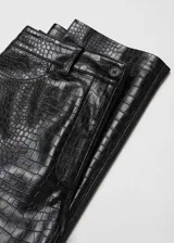 Pantalón negro de viscosa con recubrimiento de poliuretano, tiro medio, corte recto, estampado animal print de cocodrilo, cierre de cremallera y botón, trabillas, dos bolsillos laterales y dos bolsillos de parche en la parte posterior.