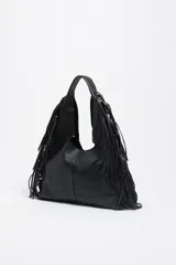 Bolso de hombro tipo hobo de piel vacuna negra, con estructura blanda, adornado con tachas metálicas circulares plateadas y flecos largos en los laterales. Presenta un asa de hombro y el logo de Bimba y Lola grabado en la parte inferior central.