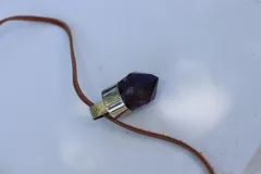 Collar con dije de amatista facetada engarzada en metal plateado, con cordón de cuero marrón.