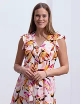 Vestido camisero midi estampado con flores en tonos rosa, naranja y marrón sobre fondo blanco. Tiene escote en V, abertura frontal con botones, mangas cortas con volados y lazo de ajuste en la cintura.