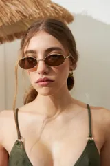 Lentes de sol con forma ovalada, montura metálica dorada y cristales marrones con protección UV.