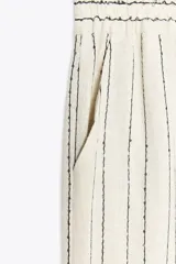 Pantalón de lino color crudo con rayas verticales negras y lentejuelas. Tiro alto con cintura elástica y bolsillos laterales.