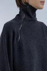 Sweater gris oscuro de lana con cuello alto y cierre asimétrico en el hombro. Presenta un calce levemente amplio y caída fluida, mangas largas con terminaciones acanaladas y aberturas laterales.