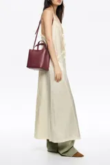 Bolso pequeño tipo tote o cubo de piel vacuna texturizada color negro, con asas cortas superiores y correa larga ajustable para llevar al hombro o cruzado. Presenta el logo metálico de Bimba y Lola en dorado en el frente.