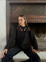 Camisa negra con cuello alto de encaje, mangas largas y cierre frontal con botones.