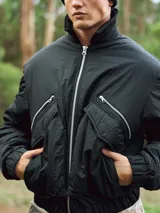 Campera bomber negra de nylon con cuello alto, cierre frontal con cremallera, bolsillos laterales con cremallera, puños y bajo acanalados.