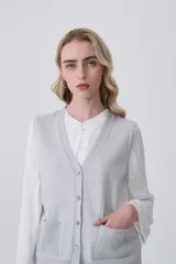 Chaleco de punto color crema, con cuello en V, cierre frontal de botones y dos bolsillos frontales.