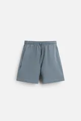 Bermuda azul de corte relaxed fit, confeccionada en tejido interlock de algodón con cintura elástica ajustable con cordón, bolsillos laterales y bolsillo trasero de plastrón.