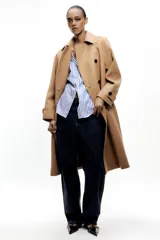 Abrigo color camel confeccionado en hilatura con lana. Tiene cuello solapa, manga larga, bolsillos delanteros ocultos en costura y cierre frontal cruzado con botones negros.