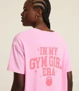 Remera deportiva oversized de malla de algodón color rosa, con cuello redondo y mangas cortas. Estampa frontal con la frase "Gym Girl" y estampa grande en la espalda.
