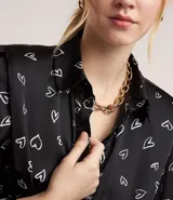 Vestido corto en crepé negro con estampado de corazones blancos, modelo chemise con hombreras y cinturón en la cintura.