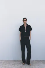 Pantalón negro de tiro medio con trabillas en la cintura, bolsillos delanteros, pierna recta y cierre frontal con cremallera, botón y gancho metálico.
