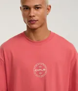 Remera relaxed de malla color salmón, con cuello redondo y mangas cortas. Estampa frontal y trasera con la palabra "EXPLR" dentro de un círculo.