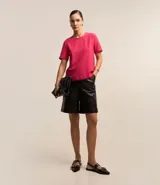 Blusa blanca de poliéster con cuello redondo, mangas cortas, cierre trasero en forma de gota, pequeñas aberturas laterales y acabados en pespuntes en las mangas y el cuello.