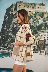 Cardigan oversized de tejido jacquard color crema con diseño de cuadrados en marrón y detalles bordados. Tiene cuello en V, cierre con botones, mangas largas y bolsillos frontales.