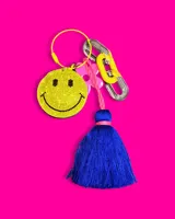 Colgante para celular con correa de silicona negra y dijes colgantes: smiley con strass, flor rosa, borla azul y cadena metálica.