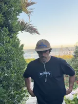 Gorra de color marrón claro con visera curva y logo bordado en azul claro en el frente.