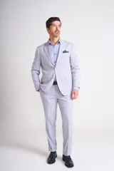 Traje de vestir celeste claro, compuesto por saco de dos botones con solapa de muesca, bolsillo de ojal en el pecho y bolsillos con solapa en los laterales, y pantalón de vestir de corte recto con ruedo arremangado.
