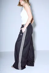 Pantalón Adidas Parachute negro de corte holgado con las tres rayas blancas a los costados.