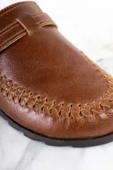 Zueco de cuero color marrón con diseño trenzado en la puntera, hebilla metálica ajustable y plantilla de corcho.