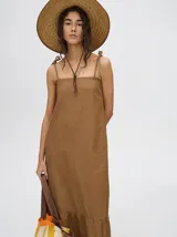 Vestido midi de denim algodón color marrón, con escote recto y tirantes finos ajustables con lazos. El corte es suelto y termina con un ruedo con semi-volado.