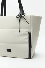 Bolso tote negro de nylon con diseño acolchado, asas largas para llevar al hombro, cierres metálicos laterales y detalle de cordón.