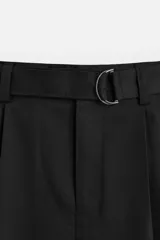 Pantalón negro de corte ancho con cinturón de tela con hebilla metálica y pliegues frontales.